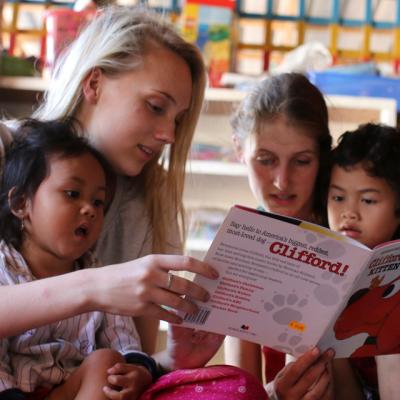 Female volunteers on the Projects Abroad Childcare Programme read a book to two local Cambodian children.