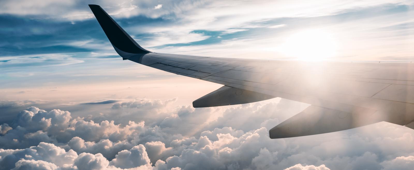 Airplane wing over cloud with sun shining.