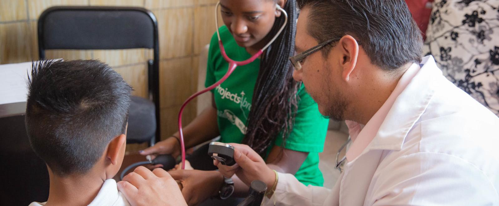 A local doctor working as a volunteer supervises a pre-med volunteer abroad during a routine health check.