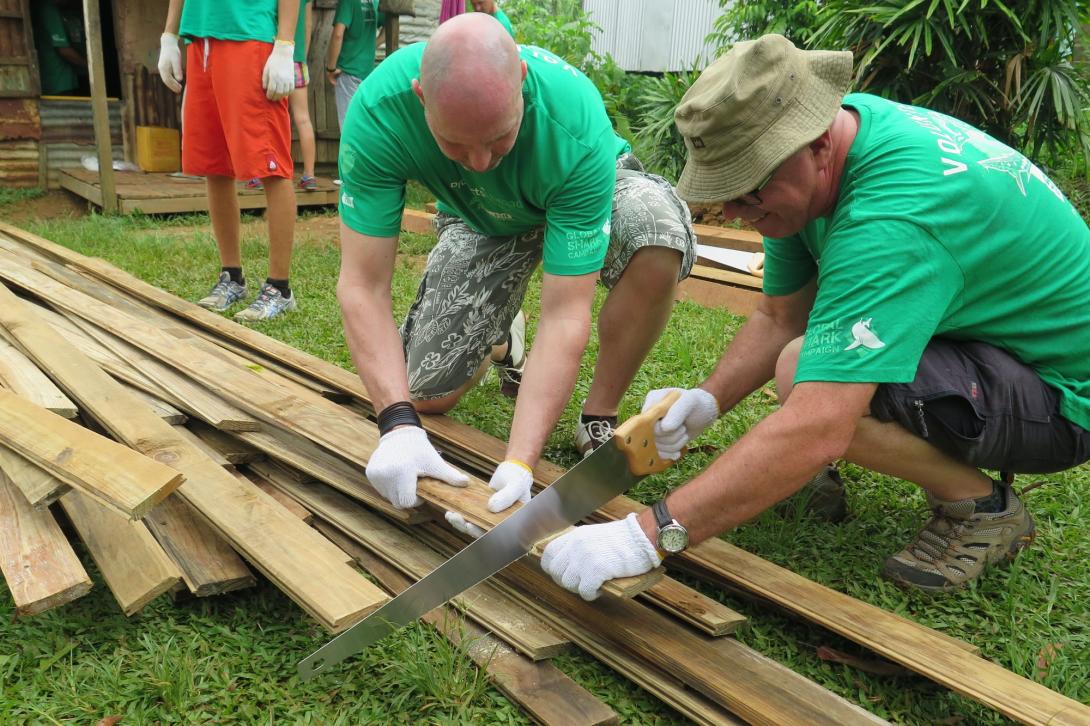 Two older Projects Abroad volunteers sawing a piece of wood as part of their building project on their gap year