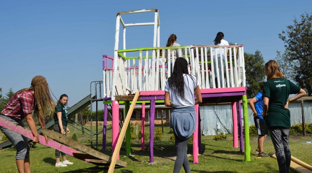 Projects Abroad volunteers working with children in Kenya help build an outdoor jungle gym with wood for a school.