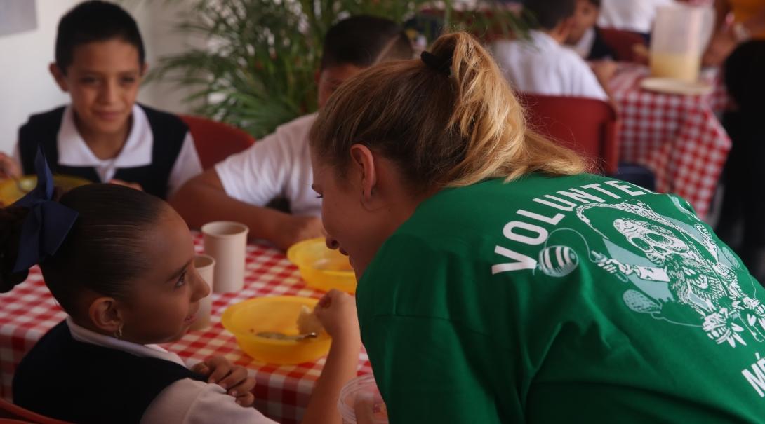 Children practice their English with a Projects Abroad Childcare volunteer while having lunch at a care centre.