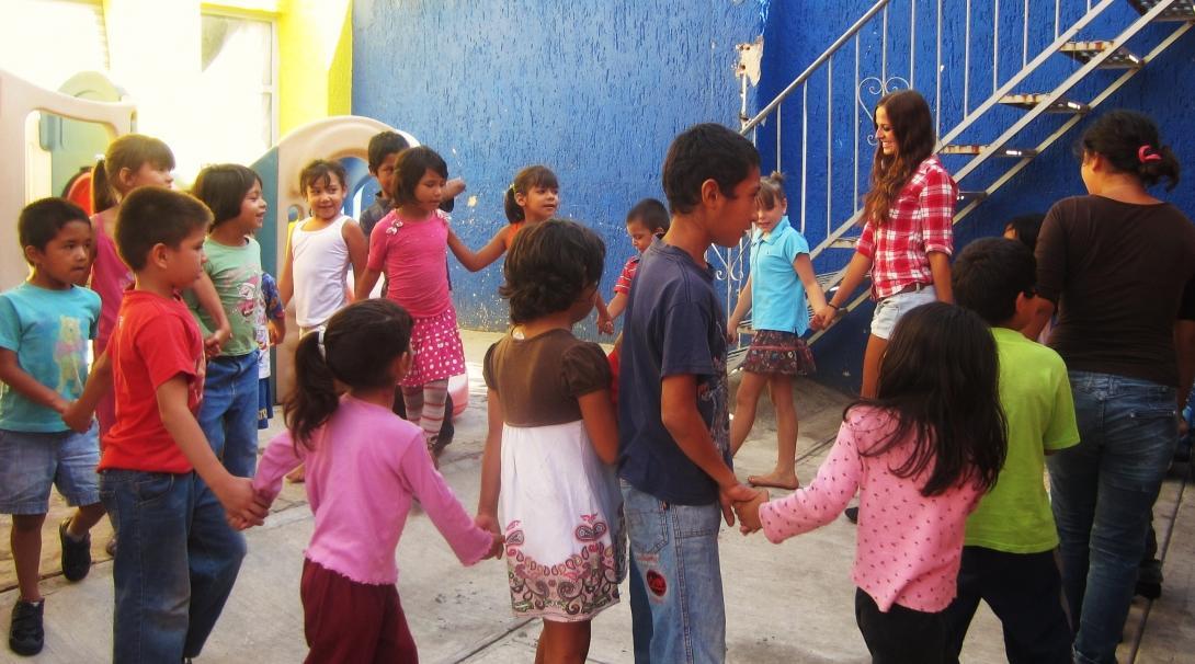 A group of Projects Abroad volunteers working with children in Mexico hold children's hands during an activity at a care centre.