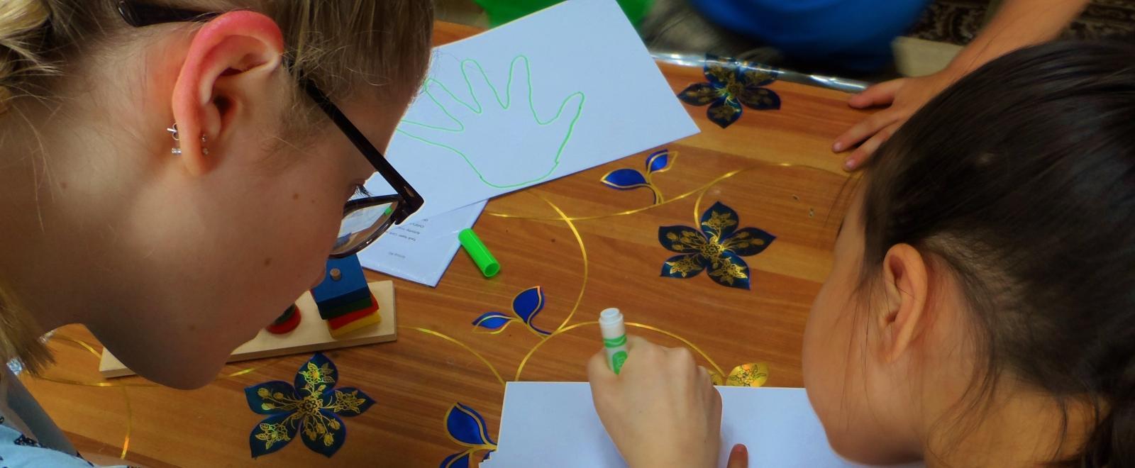 Projects Abroad volunteer working with children in Mongolia helps a child draw around their hands during an educational acitivity.