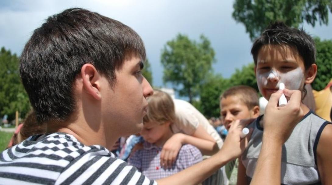 Projects Abroad volunteer with children in Romania paints a child's face during an outdoor activity at a Childcare placement.