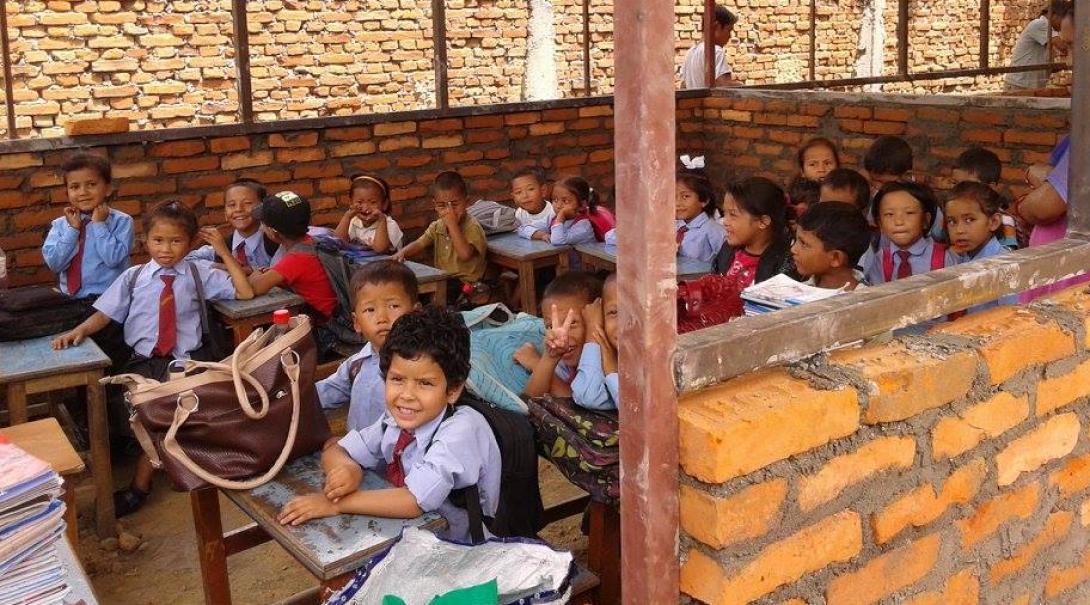 Female Projects Abroad volunteer takes a picture of a group of children having a lesson in a half built classroom whilst on her building volunteer work in Nepal.