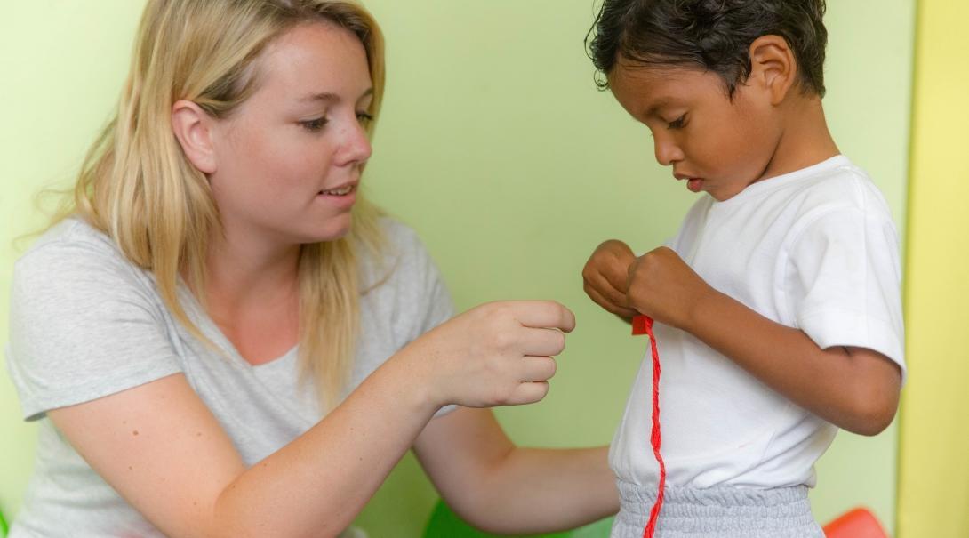 Projects Abroad volunteer working with children in Ecuador helps child with an activity in a day care centre.