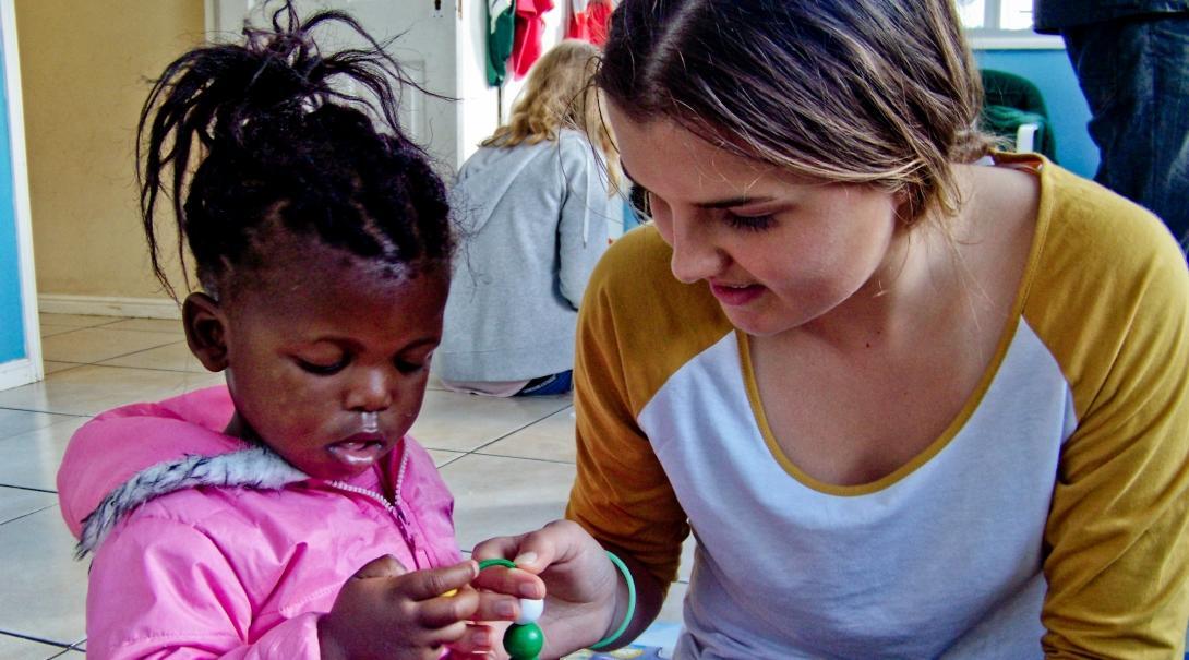 Projects Abroad Childcare volunteer helps a young child withs crafts in South Africa.