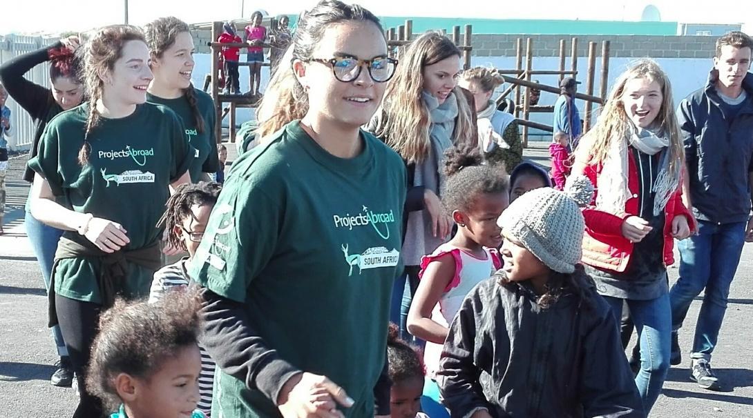 Female volunters with children in South Africa hold hands of local children and lead them on a walk at their Childcare Project. 