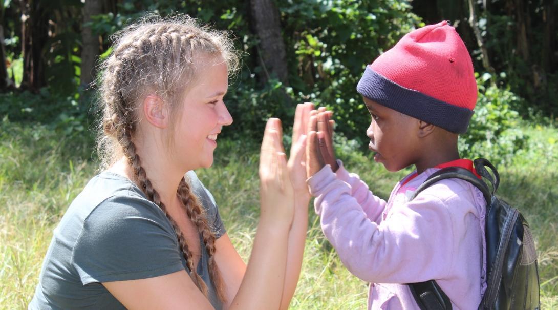 Female volunteer working with children in Tanzania high fives a young boy outside a care centre.