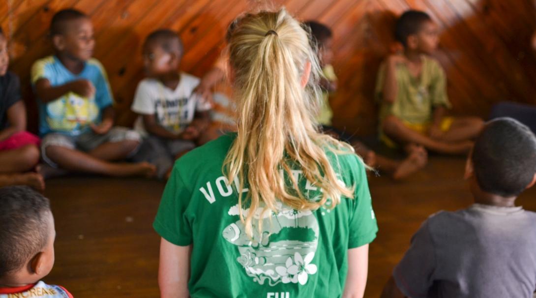 Female Culture and Community volunteer sits in a circle with school children in a Day Centre during a Community Project in Fiji.