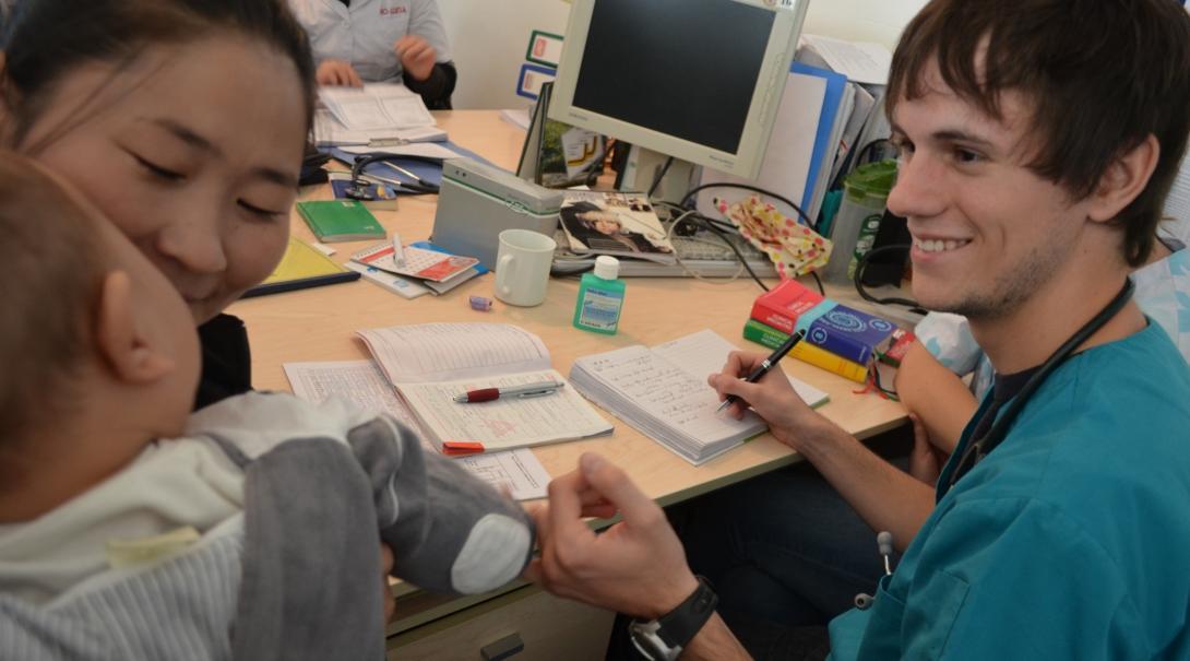 Male medical intern sits down with a local woman and her baby during an examination held in Mongolia. 