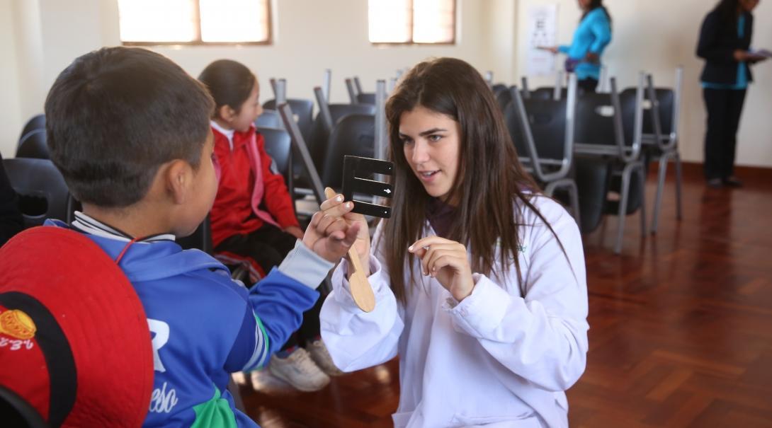 A female Projects Abroad intern explians an eye test to a local child whilst on her medical internship in Peru.