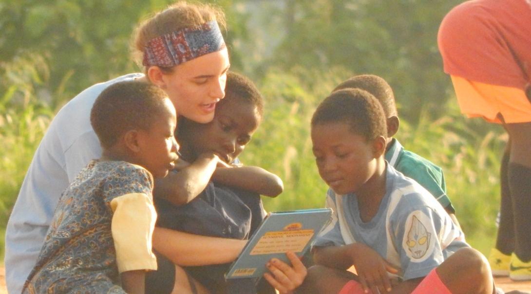 While doing community volunteer work in Ghana, a teenager sits on the floor, reading a book to her students. 