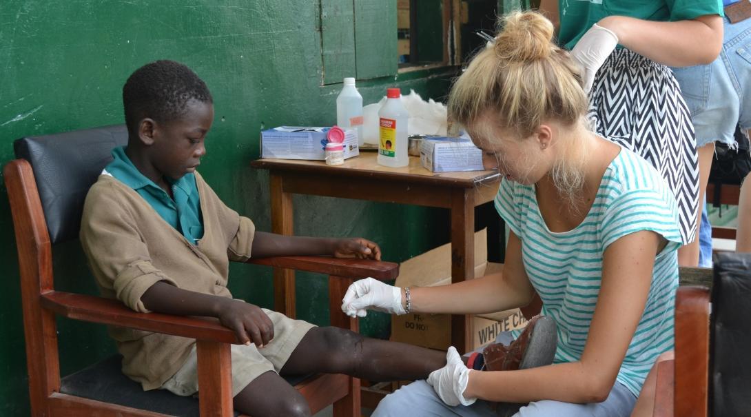 Projects Abroad Nursing intern in Ghana cleans a child's wound during an outreach at his school.