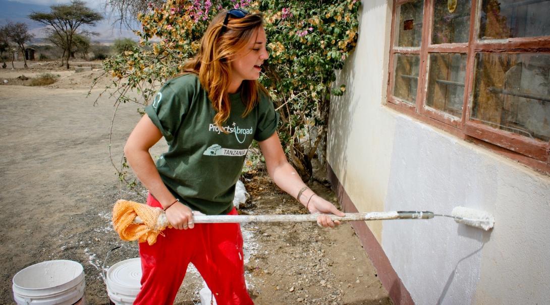 A teenage volunteer doing construction work in Tanzania paints a wall white.  