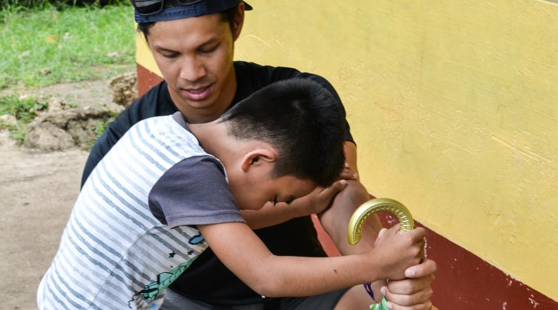 A male intern at Projects Abroad assisting a child with walking and straightening his legs whilst on his physiotherapy internship in the Phillippines.