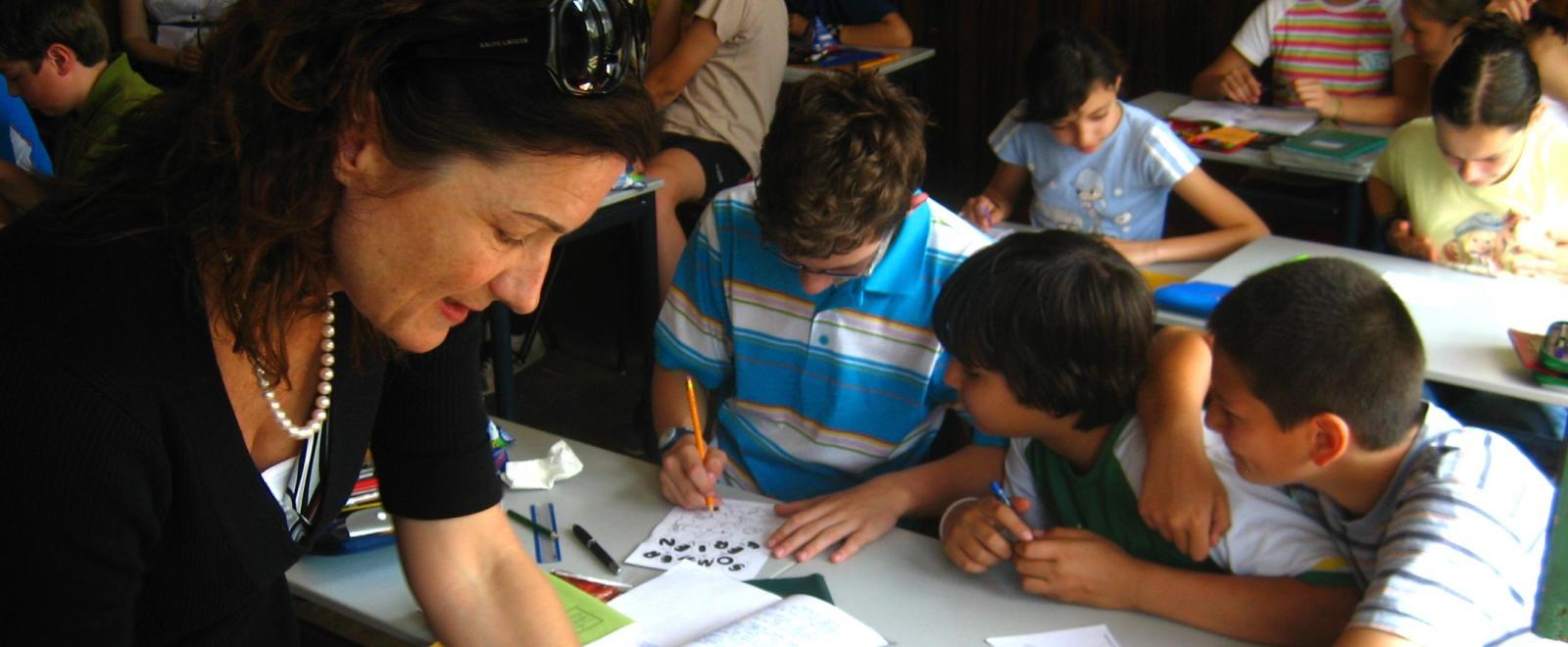 Students listen to a young Teaching volunteer in Romania while an older volunteer prepares for the lesson