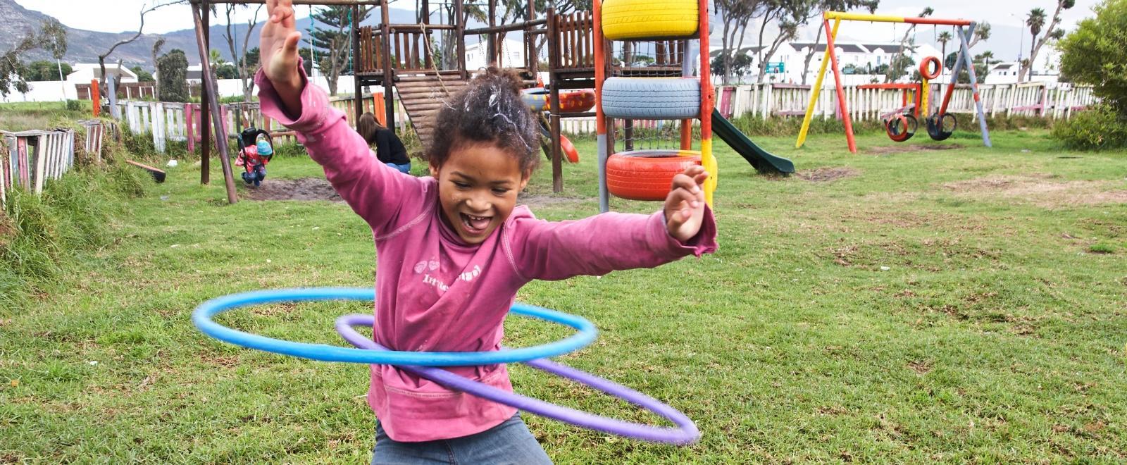 During a Childcare Project in South Africa, a young girl hula hoops outside a care centre.