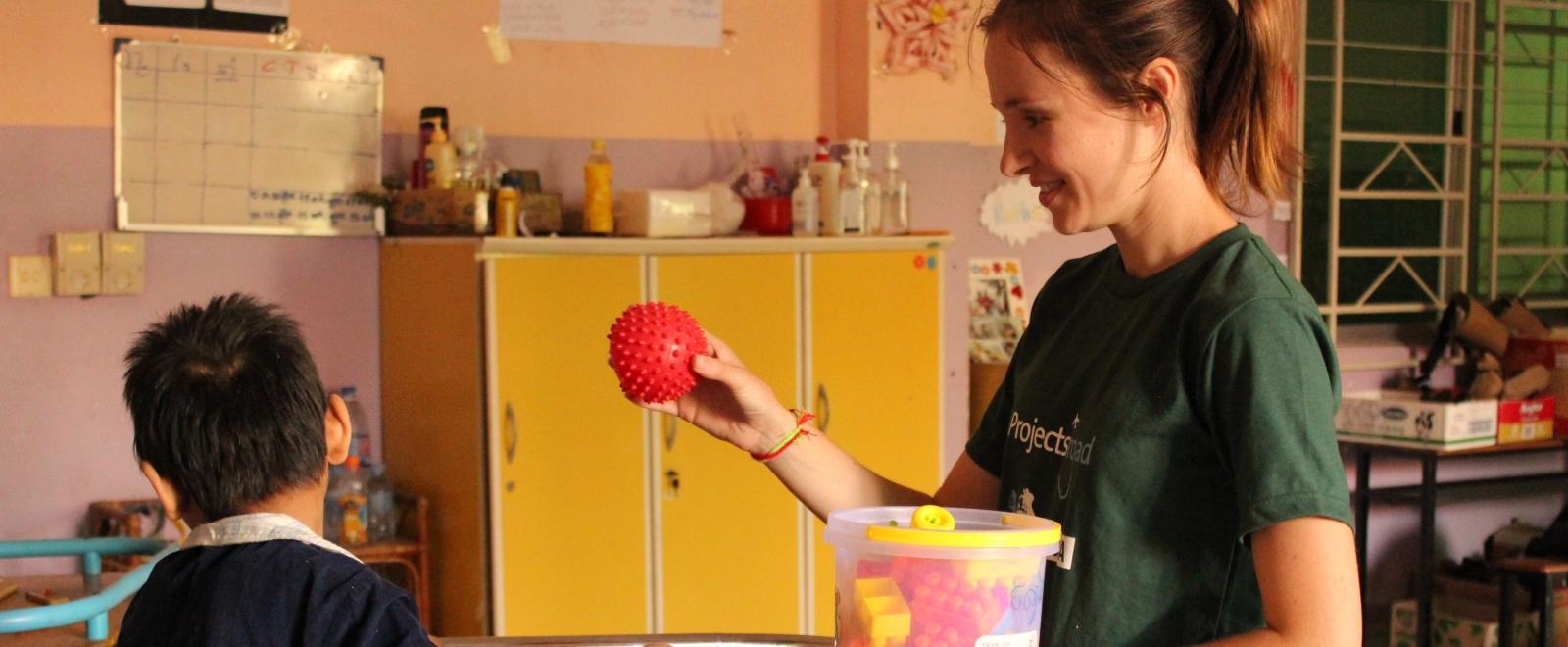 A disabled child does basic exercises using a ball with a student doing an Occupational Therapy internship abroad.