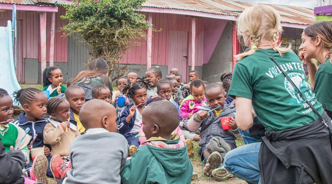 Volunteers talk with the children while they are eating as they complete volunteer work with children for teenagers in Kenya. 