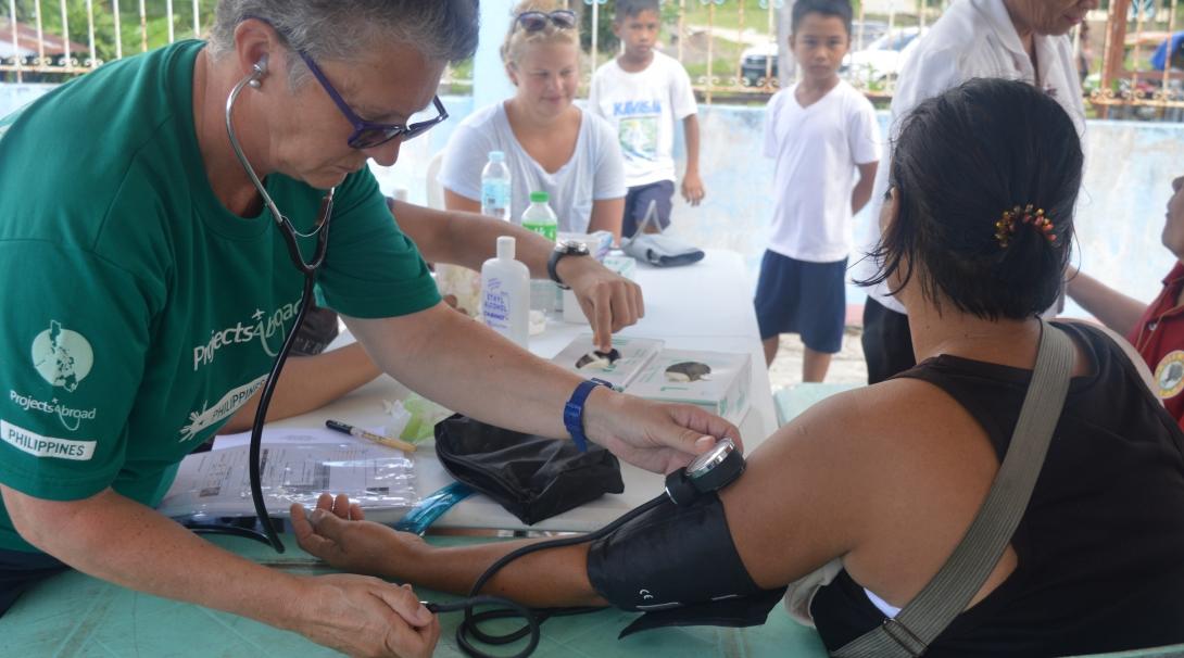 A woman participating in a volunteer abroad program for older adults in the Philippines helps a young woman at an outreach. 