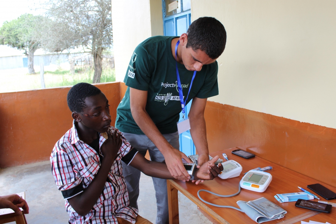 A teen measuring a patient’s blood pressure during his medical project for high school students.