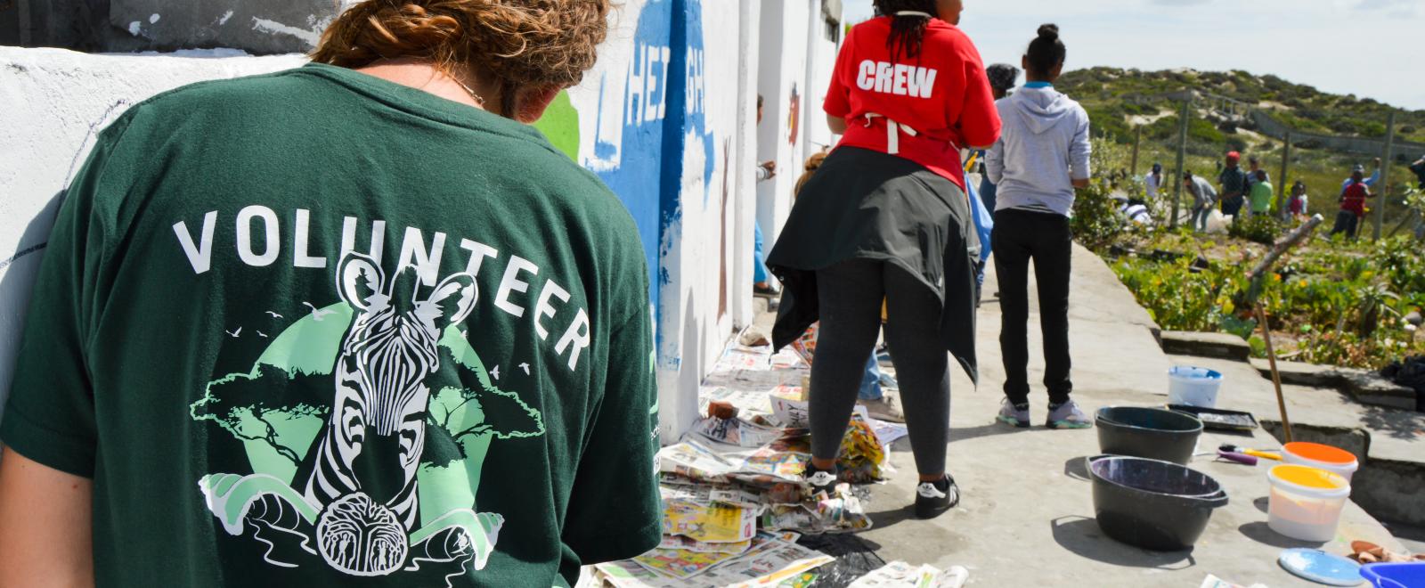 A volunteer paints a mural on a school wall during her volunteer work abroad