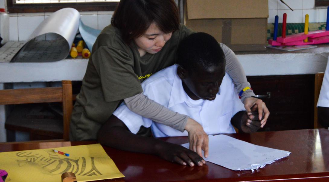 A Projects Abroad volunteer doing a physiotherapy internship in Ghana helps a young student to recover movement in his arms and hands.