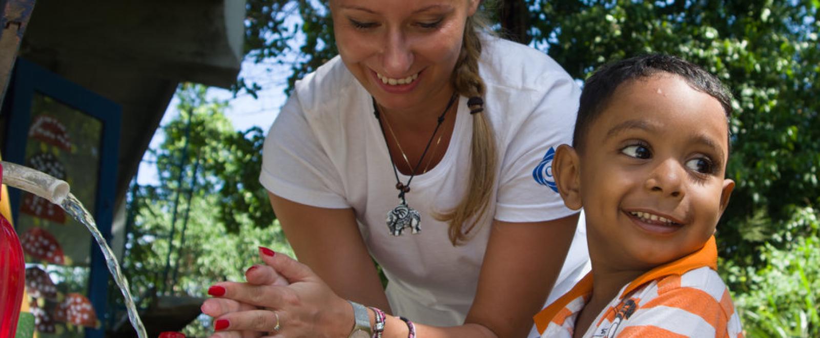 A volunteer from a corporate group trip helps a child wash his hands in Sri Lanka. 